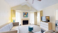 This thoughtfully designed suite offers 3 bedrooms and 3 bathrooms across a single floor, providing a comfortable and functional layout. The living room is the architectural centerpiece, featuring soaring vaulted ceilings, a ceiling fan, and a tile-surround fireplace framed by sheer and patterned drapery that filters generous natural light. Contemporary furnishings, a flat-screen TV, and colorful wall art create a welcoming, relaxed ambiance throughout.

The fully equipped kitchen is both practical and stylish, showcasing stainless steel appliances including a refrigerator, range, microwave, and dishwasher, complemented by warm maple cabinetry, granite countertops, a tiled floor, and a breakfast bar for casual dining.

Each bedroom is designed for restful comfort, offering clean, light-toned décor with soft blue accent walls, light wood headboards with integrated nightstands, and large windows dressed with layered curtains for flexible light control. The primary bedroom is notably spacious, providing ample room to relax.

The bathrooms are clean and efficiently designed, featuring tub-shower combinations with marble-style surround panels and wood-look flooring, maintaining a consistent neutral palette throughout. The overall atmosphere of the suite is bright, airy, and inviting, blending residential comfort with well-considered design details.