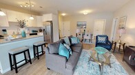 Located at 9 Covered Bridge Rd, this single-floor residence offers a thoughtfully designed open-concept layout with light hardwood-style flooring throughout. The living area is generously sized, featuring large sliding glass doors that open to a private balcony, allowing natural light to fill the space. A dedicated dining area accommodates a full-sized table for four and is accented by a window with tasteful drapery. The kitchen is well-equipped with white shaker cabinetry, granite countertops, a subway tile backsplash, stainless steel appliances including a gas range, dishwasher, and French door refrigerator, plus a peninsula with bar seating. The bedrooms are comfortably proportioned with large windows, ample closet space, and light-toned walls that create a calm, restful atmosphere. The primary bedroom includes a dedicated en-suite bathroom featuring a single-sink vanity with white countertops and a glass-enclosed shower. Throughout the residence, a cohesive coastal-inspired color palette of teal, navy, and neutral tones lends the space a polished, welcoming character. The overall layout is efficient and functional, providing a comfortable living environment with modern finishes.