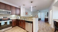 This thoughtfully designed 1-bedroom, 2-bathroom residence offers a functional and stylish single-floor layout. The open-concept kitchen and living area serves as the heart of the home, where rich dark-wood cabinetry, granite countertops, a subway tile backsplash, and a full suite of stainless steel appliances — including a refrigerator, range, microwave, and dishwasher — create a polished and practical culinary space. A peninsula with pendant lighting provides additional prep space and a natural divider between the kitchen and living area. The living room features warm hardwood-style flooring, a ceiling fan, and large sliding glass doors that fill the room with natural light and provide access to the outdoors. The primary bedroom is a comfortable retreat, complete with hardwood-style flooring and a walk-in closet offering built-in shelving and hanging space. The primary bathroom is well-equipped with dual sinks set in granite countertops atop dark wood cabinetry, a large mirror, and a soaking tub. A hallway connects the main living spaces and provides access to additional storage. Throughout the residence, a consistent palette of light walls, warm wood tones, and modern fixtures creates a cohesive and inviting ambiance.