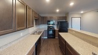This single-floor residence at 6300 E 45th St in Sioux Falls, South Dakota, offers a thoughtfully designed layout with a cohesive, contemporary aesthetic. The kitchen serves as a functional centerpiece, featuring rich dark-stained cabinetry extending to the ceiling, light granite-style countertops, a double-basin sink, and black appliances including a range, over-the-range microwave, dishwasher, and refrigerator. Recessed lighting illuminates the space, while durable wood-look flooring adds warmth and practicality. A peninsula provides additional counter space and a natural division between the kitchen and adjoining areas.

The bedrooms are finished with neutral-toned carpet and soft grey walls, each offering a window that allows natural light to filter in. One bedroom overlooks neighboring buildings, while another enjoys a more open, green outdoor view.

The bathroom is well-equipped with a wide vanity topped with speckled countertops, a large wall mirror, a lighted vanity bar, and a walk-in shower with white surround. Wood-look flooring continues here, complementing the dark cabinetry. A hallway bathroom area features additional built-in cabinetry for storage. The overall design maintains a clean, modern character with consistent finishes throughout.