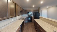 This single-floor residence at 6300 E 45th St in Sioux Falls, South Dakota, offers a thoughtfully designed layout with a cohesive, contemporary aesthetic. The kitchen serves as a functional centerpiece, featuring rich dark-stained cabinetry extending to the ceiling, light granite-style countertops, a double-basin sink, and black appliances including a range, over-the-range microwave, dishwasher, and refrigerator. Recessed lighting illuminates the space, while durable wood-look flooring adds warmth and practicality. A peninsula provides additional counter space and a natural division between the kitchen and adjoining areas.

The bedrooms are finished with neutral-toned carpet and soft grey walls, each offering a window that allows natural light to filter in. One bedroom overlooks neighboring buildings, while another enjoys a more open, green outdoor view.

The bathroom is well-equipped with a wide vanity topped with speckled countertops, a large wall mirror, a lighted vanity bar, and a walk-in shower with white surround. Wood-look flooring continues here, complementing the dark cabinetry. A hallway bathroom area features additional built-in cabinetry for storage. The overall design maintains a clean, modern character with consistent finishes throughout.