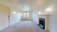 Located at 1926 Market Ave N in Canton, Ohio, this single-floor property offers a thoughtfully laid-out interior with a blend of classic architectural details and functional living spaces. The main living area serves as a focal point of the home, highlighted by an elegant fireplace with a white-painted wood mantel and brass-accented surround, flanked by wall sconce lighting that adds a warm, traditional ambiance. Soft carpeting and a textured ceiling with crown molding complete the room's classic character, while a window offers pleasant views of the surrounding greenery. An additional spacious room features a ceiling fan, wall sconces, and direct access to a hallway, providing flexible use as a living or dining area. The bedrooms are generously sized with plush carpeting, natural light streaming in through multiple windows, and convenient closet storage. The kitchen is equipped with white cabinetry featuring decorative scalloped trim, ample counter space, a double stainless steel sink, and tile flooring, with a door providing direct exterior access. Throughout the home, radiator heating units are present beneath the windows, reflecting the property's enduring construction. The overall layout, visible in the dollhouse view, reveals a well-connected floor plan suited for comfortable everyday living.