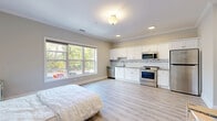 Located at 320 Howe Ave in Shelton, Connecticut, this thoughtfully designed single-floor unit offers a compact yet functional open-concept layout that maximizes every square foot. The combined living, dining, and kitchen area forms the heart of the space, characterized by light-toned luxury vinyl plank flooring and neutral warm-gray walls accented by clean white crown molding throughout.

The kitchen is a standout feature, outfitted with crisp white shaker-style cabinetry, granite countertops, a white subway tile backsplash with a mosaic glass tile accent strip, and a full suite of stainless steel appliances including a range, over-the-range microwave, dishwasher, and refrigerator. A large window floods the living and sleeping area with natural light while offering views of the surrounding greenery, contributing to an airy and bright ambiance.

The bathroom features wood-look porcelain tile flooring, clean white walls, and a walk-in shower, providing a calm and functional space. A dedicated closet offers convenient storage, and an in-unit laundry area adds everyday practicality. The overall design is modern and move-in ready, with consistent finishes and recessed lighting that create a cohesive, well-appointed living environment.