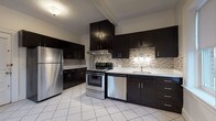 Located at 156 Maple St in Springfield, MA, this single-floor space offers a well-balanced combination of modern updates and classic architectural details. The kitchen serves as a standout feature, showcasing dark espresso cabinetry that extends to the ceiling for ample storage, white countertops, and a mosaic tile backsplash in neutral tones. Stainless steel appliances — including a refrigerator, electric range, and dishwasher — complement the sleek design, while large white tile flooring adds a clean, bright finish. A window provides natural light and an outdoor view, enhancing the kitchen's open feel.

The living areas and bedrooms feature warm hardwood flooring throughout, contributing to a cohesive and inviting ambiance. Rooms are generously proportioned with crisp white walls and large windows fitted with roller shades, allowing for ample natural light and views of the surrounding neighborhood. A drop tile ceiling in one of the living areas adds a distinct architectural element.

A long hallway with continuous hardwood flooring connects the rooms efficiently. The bathroom is finished with full white tile walls and flooring, a soaking tub, and a window overlooking the outdoors, creating a clean and functional space.