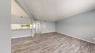 This thoughtfully laid-out one-bedroom, one-bathroom unit spans a comfortable single floor, offering an efficient and functional living space. Consistent wood-look luxury vinyl flooring flows throughout, complemented by soft gray walls and white baseboards that create a clean, cohesive aesthetic. The open-concept living and dining area is generously proportioned, providing ample room for both relaxing and entertaining. Textured ceilings add character, while multiple windows fitted with blinds allow natural light to brighten the space. The galley-style kitchen is equipped with warm wood-toned cabinetry, a double-basin sink, a dishwasher, and white appliances including a refrigerator and range. A dedicated dining area sits adjacent to the kitchen, defined by a countertop pass-through. The spacious primary bedroom is well-sized and features a window for natural light. A large walk-in closet with dual hanging rods provides abundant storage. The bathroom includes a wide vanity with granite-look countertops, white cabinetry, a large mirror, and a tiled soaking tub and shower combination. The unit also benefits from central HVAC vents throughout, ensuring year-round comfort.
