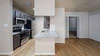 Located at 3009 Ira Young Dr in Temple, Texas, this single-floor residence offers a well-designed layout that balances functionality and modern finishes throughout. The kitchen is a standout feature, equipped with dark espresso-toned cabinetry, granite countertops, a full suite of stainless steel appliances including a range, microwave, and refrigerator, and a white subway tile backsplash. Light wood-style flooring runs through the kitchen and main living areas, adding warmth and cohesion. A peninsula with a granite countertop and built-in sink extends into the adjoining space, creating a natural flow between the kitchen and living areas. The bedrooms feature plush carpeting and are bathed in natural light through sizable windows with blinds. Each bedroom offers generous proportions, with at least one room featuring a closet with built-in shelving. The bathroom is finished with a granite-top vanity, dark cabinetry with a matching overhead cabinet, a large mirror, and a tub-shower combination enclosed by a curved curtain rod with marble-look tile surround. Textured ceilings are present throughout the unit. The overall ambiance is clean, contemporary, and move-in ready.