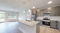 This thoughtfully designed 2-bedroom, 2-bathroom residence in Rochester, MN offers a well-appointed single-floor layout with modern finishes throughout. The open-concept kitchen serves as the heart of the home, showcasing a large granite-topped island with an undermount sink, pendant lighting, gray shaker-style cabinetry, a white subway tile backsplash, and a full suite of stainless steel appliances. Light wood-tone flooring flows through the main living areas, connecting the kitchen seamlessly to the living room, which benefits from natural light through generous windows. The spacious primary bedroom features direct access to a private balcony with outdoor views, a walk-in closet, and an en suite bathroom equipped with a walk-in shower, gray cabinetry, and granite countertops. The second bedroom is carpeted and bright, with a large window overlooking the surrounding greenery. The second bathroom includes a full soaking tub and shower combination, a granite-topped vanity with ample storage, and matching gray cabinetry. Additional conveniences include in-unit laundry and a utility room. The overall aesthetic is clean, contemporary, and neutral, offering a move-in-ready living environment.