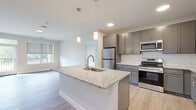 This thoughtfully designed 2-bedroom, 2-bathroom residence in Rochester, MN offers a well-appointed single-floor layout with modern finishes throughout. The open-concept kitchen serves as the heart of the home, showcasing a large granite-topped island with an undermount sink, pendant lighting, gray shaker-style cabinetry, a white subway tile backsplash, and a full suite of stainless steel appliances. Light wood-tone flooring flows through the main living areas, connecting the kitchen seamlessly to the living room, which benefits from natural light through generous windows. The spacious primary bedroom features direct access to a private balcony with outdoor views, a walk-in closet, and an en suite bathroom equipped with a walk-in shower, gray cabinetry, and granite countertops. The second bedroom is carpeted and bright, with a large window overlooking the surrounding greenery. The second bathroom includes a full soaking tub and shower combination, a granite-topped vanity with ample storage, and matching gray cabinetry. Additional conveniences include in-unit laundry and a utility room. The overall aesthetic is clean, contemporary, and neutral, offering a move-in-ready living environment.