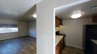 This single-floor space showcases a practical and straightforward layout, with an open connection between the kitchen and living area that promotes a sense of flow. The kitchen is equipped with warm medium-toned wood cabinetry, a black gas range with an overhead ventilation hood, and light-colored countertops that provide a clean contrast to the darker elements in the space. A textured white column serves as a partial divider between the kitchen and the adjacent living area, adding architectural definition without fully closing off the space. The living area is open and unobstructed, with neutral gray walls and dark hardwood-style flooring that extends throughout both areas, contributing to a cohesive and grounded aesthetic. Flush-mount ceiling light fixtures provide consistent overhead illumination in each area. Textured white ceilings and walls add subtle visual interest throughout. The overall ambiance is functional and understated, offering a clean, move-in-ready environment with a neutral palette that provides a versatile backdrop for a variety of interior styles.