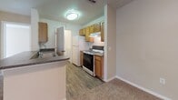 Located on a quiet cove in Tarpon Springs, Florida, this single-story home offers a practical and comfortable layout designed for everyday living. The kitchen is equipped with warm honey-toned wood cabinetry, a gas range, a full-size refrigerator, and a double sink with a breakfast bar peninsula, with wood-look flooring that transitions into the carpeted living areas. The spacious living room features a ceiling fan with light kit, neutral beige walls, and natural light streaming through a large window with views of surrounding greenery. Multiple bedrooms continue the warm, neutral palette, each finished with plush carpet, ceiling fans, and windows that bring in natural light. Several bedrooms include closets with wire shelving for organized storage. The bathrooms are clean and bright, each featuring a full tub-shower combination with white tile surround and a toilet; one bathroom also includes a vanity with a granite-style countertop. A dedicated laundry area houses a full-size washer and dryer with overhead shelving for added utility. Throughout the home, the consistent use of neutral tones, carpet, and ceiling fans creates a cohesive and livable atmosphere well-suited to the warm Florida climate.