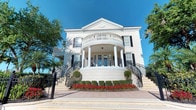 This distinguished neoclassical structure commands immediate attention with its striking white façade, symmetrical design, and refined architectural detailing. The exterior presents a dramatic curved portico supported by tall, classical columns that frame the main entrance, which is accessed via dual sweeping staircases adorned with wrought-iron railings. A decorative pediment crowns the roofline, while a curved upper-level balcony enclosed by a white balustrade extends gracefully over the portico below, adding depth and grandeur to the elevation. Black-shuttered windows punctuate the façade, providing strong contrast against the crisp white exterior. The entry level is thoughtfully landscaped with neatly trimmed boxwood hedges, vibrant red flowering plants, and ornamental topiaries that enhance the formal, manicured aesthetic. Mature trees flank the building on either side, softening the grand scale with natural greenery. The overall design evokes a sense of timeless elegance and institutional prestige, drawing from Southern and Beaux-Arts architectural traditions. The generous proportions, layered terracing, and meticulous detailing collectively create a space that is both visually impressive and architecturally significant.