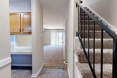Located at 132 Tide Mill Ln in Hampton, Virginia, this two-story home offers a well-organized layout divided equally between its two floors. The main level features a kitchen equipped with warm honey-toned wood cabinetry, light speckled countertops, black appliances including a range and dishwasher, and durable wood-look flooring. Adjacent to the kitchen, a hallway connects to the carpeted living room, which is bathed in natural light and provides direct outdoor access through a sliding glass door with vertical blinds opening to a green outdoor area. A staircase with a metal railing leads to the upper level, where both bedrooms are found. The spacious primary bedroom includes plush carpeting, a ceiling fan with light fixture, and a dedicated closet. The second bedroom also features carpet flooring, a ceiling fan, and natural light from a window with horizontal blinds offering outdoor views. A full bathroom on the upper floor includes a white vanity with ample storage, a tiled tub-shower combination, and wood-look vinyl flooring. Three closets throughout the home provide generous storage. The neutral color palette and carpet-and-hardwood flooring combination create a clean, functional living environment throughout.