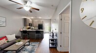 Located at 1849 W Gordon St in Remerton, GA, this 2-bedroom, 2-bathroom single-floor residence offers a practical and well-designed layout. The open-concept living and kitchen area serves as the heart of the home, where a peninsula counter with bar seating connects the two spaces. The kitchen is outfitted with modern two-tone cabinetry, granite-style countertops, black appliances including a refrigerator, range, and over-the-range microwave, and warm hardwood-style flooring that extends throughout the unit. A ceiling fan anchors the living area, which offers comfortable room for a sofa and coffee table arrangement. Both bedrooms are well-proportioned, featuring hardwood-style floors, ceiling fans, and windows with blinds that allow natural light. The primary bedroom includes a double-door closet and multiple windows, while the second bedroom also features built-in drawer storage beneath the window. Each bedroom is served by its own full bathroom, both finished with granite-top vanities, full-size tub-shower combinations, and neutral grey walls. The clean, consistent color palette of soft grey walls and white trim throughout creates a cohesive and contemporary ambiance.