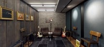 This music rehearsal studio is a well-appointed single-level space designed to balance acoustic performance with stylish, inspiring aesthetics. The room features a striking contrast of materials throughout: large teal-toned acoustic panels framed in dark trim line portions of the walls, effectively managing sound, while a dramatic dark-stained vertical wood plank wall serves as a focal point adorned with four framed music-themed artworks — including iconic album covers and artist portraits — lending the space a gallery-like character.

The flooring consists of warm hardwood planks, partially covered by a dark patchwork area rug that anchors the central rehearsal zone. The studio is equipped with practical yet quality instruments and gear, including electric guitars on stands, a Marshall combo amplifier, and a Yamaha digital keyboard on a stand, making the space immediately ready for use.

A dedicated lounge area features two low-profile brown leather chairs flanking a floor lamp with an industrial aesthetic, set against an exposed brick-style wall — creating a relaxed environment for listening or collaborating. Track lighting and linear LED fixtures illuminate the space evenly, contributing to the studio's polished, creative ambiance.