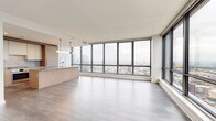 Located in Chicago's vibrant West Loop neighborhood, this single-floor high-rise residence offers a refined contemporary living experience defined by clean lines, premium materials, and breathtaking panoramic city views. Floor-to-ceiling windows wrap the open-concept living and dining area, flooding the space with natural light and framing expansive views of the Chicago skyline and surrounding neighborhoods. Light-toned hardwood flooring flows throughout, enhancing the bright, airy ambiance.

The chef's kitchen is outfitted with flat-front light oak cabinetry, stone countertops with a matching backsplash, stainless steel appliances including a gas cooktop and wall oven, and a built-in wine refrigerator — all centered around a generous island ideal for both prep and entertaining.

Bedrooms continue the floor-to-ceiling window theme, offering city views and ample built-in closet storage with custom shelving. A dedicated walk-in closet provides additional organization space. The bathrooms are thoughtfully designed: a full bath features a soaking tub, tiled shower with glass enclosure, and light wood-look flooring, while additional bathrooms showcase warm oak vanities with stone counters and sleek concrete-finish vanities with matte black fixtures. A well-organized corridor with louvered utility doors completes the layout.