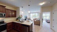 This thoughtfully designed single-floor residence offers a seamless blend of functionality and comfort across its open-concept layout. The kitchen serves as a central hub, showcasing rich dark wood cabinetry, light quartz countertops, stainless steel appliances including a range, microwave, dishwasher, and refrigerator, and a large island with an undermount sink and bar seating. Elegant pendant lighting illuminates the island, while hardwood-style flooring anchors the space.

The kitchen flows naturally into a combined dining and living area, where plush carpeting, generous natural light, and a sliding glass door lead to a private balcony overlooking lush greenery. The living room offers a relaxed, open ambiance with ample room for comfortable seating arrangements.

The bedroom is a serene retreat, featuring soft carpeting, large windows with calming outdoor views, and a dedicated walk-in closet providing substantial storage. The full bathroom is finished with slate-style tile flooring, a dark double-vanity with white countertops, a large mirror, and a full tub-shower combination, offering a clean and polished aesthetic throughout.