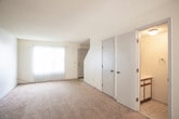 This two-story residential space is designed with functionality and practicality in mind. The layout spans two floors, offering a well-organized flow between living, sleeping, and utility areas.

The kitchen is equipped with white cabinetry featuring wood-tone trim, and includes black appliances—an electric range, over-the-range microwave, and refrigerator. Light tile flooring runs through this area, and a window provides natural light alongside a secondary entry door.

The main living area is generously sized, featuring wall-to-wall carpet and a large window dressed with vertical blinds that invite natural light into the room. A pass-through opening connects the living space to the kitchen, enhancing the overall sense of openness.

Additional carpeted rooms serve as bedrooms, each featuring sliding-door closets with built-in shelving and windows that bring in daylight. One room benefits from a staircase nearby, indicating its position on the lower level, while upper-level rooms offer a quieter setting.

The full bathroom includes a tub-shower combination with a tile surround, toilet, and a vanity with under-sink storage. Light tile flooring completes the clean, functional look of this space throughout its wet areas.