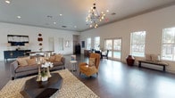 This single-story leasing office is designed to be both functional and inviting, combining open-concept layout with contemporary styling. The main reception area is expansive and airy, featuring soaring ceilings accented by a striking multi-bulb sputnik chandelier that serves as a central design focal point. Dark hardwood-style flooring runs throughout, providing a clean, polished foundation that complements the crisp white walls and crown molding details.

The lounge area is furnished with a caramel leather accent chair, a gray upholstered sofa, a patterned area rug, and side tables, creating a comfortable and welcoming environment for prospective residents. Large windows and French doors flood the interior with natural light while offering outdoor views of the surrounding property, including a pool area. A wall-mounted flat-screen television and compact storage cabinet provide additional utility within the space.

The dedicated office workstation area is positioned near the windowed perimeter, outfitted with a dark wood L-shaped desk, dual monitors, and filing storage — designed to support leasing staff efficiently. Additional decorative wall art and accent pieces contribute to the professional yet approachable ambiance throughout the office.