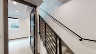Located at 552 N Hobart Blvd in the heart of Los Angeles, this modern two-story unit showcases a clean, contemporary design throughout. The main level features light wood-look flooring that flows across an open-plan living and kitchen area. The kitchen is outfitted with sleek, high-gloss white upper cabinets, dark lower cabinets, stainless steel appliances including a refrigerator and dishwasher, and a metallic tile backsplash that adds a stylish accent. Recessed lighting throughout ensures a bright, well-lit atmosphere. A striking black spiral staircase serves as a focal architectural centerpiece on the main level, complemented by a black metal railing that lines the upper landing. The second floor offers carpeted bedrooms with large black-framed windows that bring in natural light. One bedroom features floor-to-ceiling mirrored sliding closet doors, enhancing the sense of space. A straight staircase with a black horizontal-rail banister connects the levels, adding to the home's cohesive modern aesthetic. The bathroom is elegantly finished with marble-look tile surrounding the tub and shower, paired with a frameless glass sliding door and polished chrome fixtures. Clean white walls and dark-framed interior doors are consistent design elements throughout, giving the space a refined, contemporary feel.