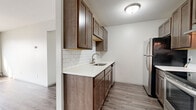 Located at 5277 W 82nd St in Bloomington, Minnesota, this single-floor unit offers a practical and well-maintained layout with a mix of updated finishes and classic details throughout.

The kitchen serves as a standout feature, showcasing rich dark-toned cabinetry extending from floor to ceiling, a clean white quartz countertop, and a white subway tile backsplash. Stainless steel appliances — including a refrigerator, electric range with overhead ventilation hood, and dishwasher — complete the space. Wood-look luxury vinyl plank flooring runs throughout the kitchen and connects seamlessly to the adjacent living areas, adding warmth and continuity.

The living area is bright and open, benefiting from a broad bank of windows that allow generous natural light to filter in. Neutral walls and clean lines give the space a versatile, move-in-ready character. A separate room features soft carpeting, gray wainscoting, a ceiling fan with light fixture, and a window with blinds, making it well-suited as a bedroom.

The bathroom is finished with white tile work, a tub-shower combination, mosaic tile flooring, a single vanity with under-sink storage, and a mirrored medicine cabinet above. Baseboard heating is present throughout the unit, and the overall layout, as visible in the floorplan view, is efficiently organized for comfortable single-floor living.