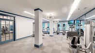 Located at 1295 Dresden Dr NE in Brookhaven, GA, this fitness center offers a comprehensively outfitted workout facility spread across a single floor with two distinct zones designed to support a wide range of fitness activities.

The main cardio and strength area features a bright, open layout defined by structural columns with navy blue accent bases that complement the facility's clean white-and-blue color scheme. Underfoot, neutral checkered carpet tile provides comfort and durability throughout the space. Large multi-pane windows line the walls, flooding the interior with natural light and offering views of the surrounding greenery. The area is equipped with a full lineup of cardio machines, including treadmills, ellipticals, stair climbers, and stationary bikes, as well as selectorized strength machines. A dedicated free weight section houses a comprehensive dumbbell rack, and flat-screen monitors are mounted for entertainment. Modern geometric pendant light fixtures add a contemporary design touch overhead.

The second zone serves as a functional training and studio space, featuring wood-style flooring and full-length mirrored walls that visually expand the room. This area is stocked with a free-standing heavy bag, kettlebells, medicine balls, resistance bands, stability balls, and a weight bench, making it ideal for dynamic, high-intensity, or group training sessions. Together, the two areas create a versatile, professionally appointed fitness environment.