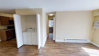 This single-floor residence offers a clean, functional layout finished with warm hardwood-style flooring that runs throughout the space, lending a cohesive and inviting feel. The neutral, light-toned walls create a bright and open atmosphere, making the interior feel airy and easy to personalize.

A standout feature of this home is the dedicated in-unit laundry area, housing a full-size side-by-side washer and dryer tucked neatly behind bifold doors — a convenient amenity that adds significant practical value. Adjacent to the laundry space, a baseboard heating unit provides reliable climate control during cooler months.

A hallway connects the main living area to additional rooms beyond, offering a clear sense of flow and separation between living and private spaces. Natural light filters through a window visible at the end of the hallway, brightening the passage and hinting at well-lit rooms throughout. The overall layout is straightforward and efficient, making good use of the available footprint while maintaining an uncluttered feel.

With its durable flooring, in-unit laundry, and simple yet functional design, this space presents a well-appointed and move-in-ready option suitable for a range of lifestyles.