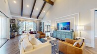 The Pointe Grand Apartment Homes clubhouse in Daytona Beach, FL, is a thoughtfully designed single-story community gathering space that blends coastal-inspired aesthetics with modern comfort. Upon entry, guests are welcomed by a bright foyer featuring herringbone-patterned hardwood flooring, bold accent wall art, and glass double doors that flood the space with natural light.

The main lounge area is anchored by soaring vaulted ceilings adorned with striking dark wood exposed beams set against white shiplap, creating a dramatic yet inviting atmosphere. Plush cream sofas, cognac leather armchairs, and a patterned area rug surround a central coffee table, while a large flat-screen television is displayed above a distinctive robin's egg blue credenza. Recessed lighting and floor lamps contribute to the warm ambiance.

An adjacent dining area features a solid wood round table with leather chairs and a large sliding glass door framed by bold blue-and-white patterned curtains, offering views of the surrounding community. A dedicated wet bar area includes a dark subway tile backsplash, built-in beverage refrigerator, coffee station, and bar seating, making it ideal for social gatherings. The overall design is cohesive, vibrant, and welcoming.