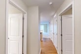 Located at 16 Cinema Dr in Lansing, NY, this single-floor, two-bedroom, two-bathroom residence offers a clean and functional layout designed for comfortable everyday living. The combined kitchen and living area serves as the heart of the home. The kitchen is well-appointed with light maple cabinetry, stainless steel appliances including a range, over-the-range microwave, and refrigerator, all complemented by white countertops and warm hardwood-style flooring that adds brightness to the space. The living room features soft carpeting and a large sliding glass door dressed with vertical blinds, allowing natural light to fill the room. A central hallway connects all areas of the home, featuring the same hardwood-style flooring and clean white panel doors with brushed metal hardware. The generously sized primary bedroom is carpeted and includes a ceiling fan with light fixture and a window offering outdoor views. The second bedroom is equally well-finished with neutral carpet and ample wall space. Both bathrooms are neatly designed, with one featuring a light wood vanity, white countertop, framed mirror, glass-panel shower enclosure, and tile flooring. Throughout, neutral wall tones, white trim, and consistent finishes create a cohesive and move-in-ready atmosphere.