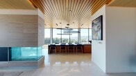 Located at 777 N Cook St in Portland, Oregon, this sophisticated single-floor space showcases a seamless blend of modern design and high-end finishes throughout. Striking wood-slat ceilings run continuously across the open layout, adding warmth and architectural depth, while polished terrazzo floors reflect abundant natural light pouring in through expansive floor-to-ceiling windows and glass walls.

The open-concept dining area features a large statement table surrounded by mid-century-inspired seating beneath a sculptural multi-arm pendant light. Floor-to-ceiling glazing frames sweeping views of Portland's treetops and skyline, creating an ever-present connection to the outdoors. A glass-enclosed fireplace serves as a dramatic central element, elegantly dividing the living and dining zones.

The kitchen is outfitted with light wood cabinetry, a striking blue tile backsplash, sleek white countertops, a deep undermount sink, and a full suite of Bosch stainless steel appliances including wall ovens and an integrated refrigerator. A generous island provides additional workspace and casual seating.

The lounge area offers a comfortable sectional, ottoman seating, a large wall-mounted display, and warm wood built-ins, with views onto a landscaped outdoor terrace. A secondary sitting nook with a blue sofa and picture window overlooks the same terrace, completing this refined and light-filled space.