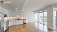 Located in the heart of downtown Durham, NC, this contemporary one-bedroom, one-bathroom residence offers a thoughtfully designed open-concept layout with clean modern finishes. The combined kitchen and living area is a standout space, anchored by expansive floor-to-ceiling sliding glass windows that frame panoramic views of the Durham skyline and surrounding cityscape, flooding the interior with natural light. Warm hardwood flooring flows throughout the main living areas, complemented by track lighting overhead. The well-appointed kitchen features white cabinetry, warm-toned countertops, a subway tile backsplash, and a full suite of stainless steel appliances including a French door refrigerator, range, microwave, and dishwasher. The spacious bedroom is finished with plush carpeting, a ceiling fan, and its own floor-to-ceiling window offering additional city views. Two closets provide generous storage. The bathroom is clean and modern, showcasing large-format white tile flooring, a wood-toned vanity with a white countertop, and a well-lit mirror. This residence delivers a bright, urban living experience with striking views of downtown Durham at every turn.