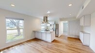 This single-floor, 2-bedroom unit offers a well-designed layout that maximizes its compact footprint. The heart of the home is an open-concept kitchen and living area bathed in natural light from multiple windows. The kitchen is a standout, featuring crisp white shaker cabinets, a granite-topped island with an integrated cooktop, a stainless steel range hood, a full-size stainless steel refrigerator, and a dishwasher — all set against light hardwood flooring that flows seamlessly through the main living space. The living area provides a generous, open feel with recessed lighting and neutral white walls that enhance brightness throughout. A hallway connects the main living space to the two bedrooms, with the primary bedroom offering a comfortable footprint alongside louvered closet doors for ample storage. The second bedroom is carpeted in a warm neutral tone, adding softness underfoot. The entry area, also finished in hardwood, features recessed lighting and a clean, welcoming layout. Throughout the unit, the design is consistent and modern, with white walls, light tones, and quality finishes that create a bright, airy, and functional living environment.