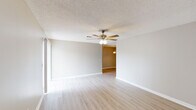 Located in Long Beach, Mississippi, this single-floor, 2-bedroom, 2-bathroom unit offers a practical and comfortable layout designed for easy living. The open living area features light wood-look flooring, neutral gray walls, a textured ceiling, and a ceiling fan with integrated lighting, creating a bright and airy atmosphere. A sliding glass door with vertical blinds floods the space with natural light and provides access to the outdoors. The living area connects seamlessly to a separate dining space, which is accented by a pendant light fixture overhead. The galley-style kitchen is well-appointed with white shaker-style cabinetry, speckled countertops, a skylight for added brightness, and black appliances including a range, microwave, and dishwasher — with light wood-look flooring continuing throughout. Both bedrooms are generously proportioned, featuring ceiling fans, neutral tones, and wood-look flooring, with one bedroom offering a window with blinds for natural light. Each of the two bathrooms includes a wide vanity with speckled countertops, a large mirror, and a shower-tub combination, with brushed nickel grab bars adding a practical touch. The unit's cohesive finishes and single-level layout make it a functional and move-in-ready space.