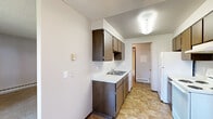 Located at 8719 N Hill N Dale St in Spokane, WA, this single-floor unit offers a functional and straightforward layout designed for comfortable everyday living. The galley-style kitchen is well-appointed with dark wood cabinetry lining both sides, white appliances including a coil-top range and refrigerator, a double-basin sink with light countertops, and tile flooring that extends through the dining area. A ceiling fan and sliding glass door in the dining space provide ventilation and direct access to a private balcony overlooking mature trees, allowing natural light to fill the area. The living room is generously sized with plush carpeting, a baseboard heating system, and a sliding glass door that further connects the interior to the outdoor balcony and wooded surroundings. The bedrooms are carpeted and equipped with ceiling light fixtures, baseboard or wall-mounted heating units, and natural light from exterior-facing windows. The full bathroom features tile flooring, a tub-shower combination with tiled surround, and a classic vanity setup. Textured ceilings are consistent throughout the unit, and dark wood interior doors add a warm, cohesive touch to the overall aesthetic.