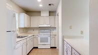 This single-story, 3-bedroom, 2-bathroom home offers a practical and comfortable layout designed for everyday living. The combined kitchen and living room serves as the heart of the home, with the living area featuring warm wood-style flooring, a ceiling fan with light fixture, a textured ceiling, and a sliding glass door that invites natural light and provides outdoor access. The kitchen is outfitted with ample white cabinetry, light countertops, a white electric range with overhead exhaust hood, a dishwasher, a full-size refrigerator, and tile flooring — providing generous storage and prep space throughout. All three bedrooms are finished with matching wood-style flooring and neutral white walls, creating bright, versatile spaces ready for personalization. The primary bedroom offers a notably generous footprint among the three. The bathrooms include a full tub-and-shower combination with built-in shelving and classic white surrounds with brushed gold fixtures. A dedicated laundry room accommodates a full-size washer and dryer side by side, complete with overhead shelving for added storage. Additional hallways and a closet contribute to the home's overall functionality and storage capacity.