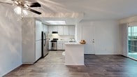 Located at 10829 Fulton Wells Ave in Santa Fe Springs, California, this single-story residence offers a well-organized layout designed for comfortable everyday living. The open-concept kitchen serves as a central highlight, featuring gray cabinetry with ample storage, light quartz-style countertops, stainless steel appliances including a gas range and full-size refrigerator, and a built-in over-the-range microwave. A peninsula with a countertop overhang provides additional workspace and a casual dining option. A skylight above the kitchen area brings in natural light, enhancing the bright, airy atmosphere. Wood-look flooring runs throughout the main living and kitchen areas, offering a clean and durable surface. The bedroom is finished with plush wall-to-wall carpeting and features a window fitted with vertical blinds, allowing natural light while maintaining privacy, with a view of the surrounding exterior greenery. A textured ceiling adds dimension to the room. The bathroom is well-appointed with a vanity featuring gray cabinetry and a single-sink countertop, a large mirror with overhead lighting, wood-look flooring, and a separate shower-tub combination enclosed by a curtain. Throughout the space, white walls and clean finishes contribute to a cohesive, move-in-ready aesthetic.