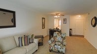 This single-floor residence offers a welcoming and functional layout that seamlessly connects the main living areas. The living room is finished with wall-to-wall carpeting that adds warmth underfoot, and features a ceiling fan with a light fixture that provides both comfort and illumination. Neutral-toned walls throughout the space create a clean, versatile backdrop suitable for a variety of interior styles. The living area flows naturally into a dedicated dining space, which benefits from a window that allows natural light to filter into the interior. A doorway visible from the main living area leads to an adjacent room, suggesting a well-connected floor plan that maximizes accessibility between spaces. The overall ambiance is calm and residential, with a straightforward layout that prioritizes ease of movement and livability. The consistent use of carpet, neutral wall colors, and practical ceiling fixtures throughout gives the space a cohesive and understated character, making it a comfortable single-level home.