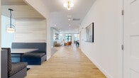 Located in Charlotte, NC, this single-story community clubhouse on Montoy Way offers a thoughtfully designed, open-concept gathering space that blends modern aesthetics with comfortable functionality. The entry corridor sets an elegant tone immediately, showcasing a striking herringbone-patterned light wood floor that flows through the main thoroughfare, complemented by crisp white walls and a stylish brass globe light fixture overhead.

The space transitions seamlessly into several distinct functional zones. A bright, carpeted lounge area features oversized sectional sofas, accent chairs, and a wall-mounted TV set against a calming sage green accent wall. Large windows flood this area with natural light and offer views of the outdoor surroundings. Adjacent to the lounge, private built-in booth seating with wood-paneled surrounds provides more intimate gathering options.

A sun-drenched sitting nook near the main entrance features rich cognac leather wing chairs, ceiling fans, and expansive windows with views of an outdoor pool area. Black-framed glass doors open directly to the exterior, enhancing indoor-outdoor connectivity.

The dining and social hub anchors the space with a substantial live-edge wood communal table, surrounded by sleek dark chairs beneath dramatic pendant lighting. A textured stone-clad feature wall hosts open shelving, a large-screen TV, and a full coffee and beverage bar, making this clubhouse as practical as it is visually impressive.