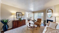 This single-floor residence offers a thoughtfully arranged layout that balances comfort and functionality across its main living spaces. The living room serves as the heart of the home, featuring a classic fireplace framed by a decorative surround, crown molding, and a textured ceiling. Large vertical-blind-covered sliding doors flood the space with natural light and connect visually to the adjacent dining area, which benefits from its own window overlooking greenery outside. The hardwood-style flooring in the dining area transitions seamlessly from the living space, creating a cohesive flow throughout.

The galley-style kitchen is efficiently organized, featuring warm honey-toned wood cabinetry, a double basin sink, light countertops, and standard appliances including an electric range and dishwasher. The hardwood-style flooring continues here, adding warmth to the compact but practical workspace.

Both bedrooms are carpeted and finished in neutral tones, offering a calm and restful atmosphere. Each room is brightened by windows with outdoor views and features ample space for furnishings. One bedroom includes access to a walk-in closet, adding practical storage. Throughout the residence, a consistent warm and neutral palette contributes to an inviting, cohesive ambiance.