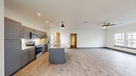 This single-floor, 2-bedroom residence offers a thoughtfully designed open-concept layout with consistent light wood-tone flooring that flows seamlessly throughout the space. At its heart is a well-equipped kitchen featuring gray shaker-style cabinetry, a full suite of stainless steel appliances, a subway tile backsplash, and a central island with granite countertops and an undermount sink, topped with a stylish pendant light. The kitchen opens directly into a generous living area with recessed lighting and a ceiling fan, creating an airy, connected atmosphere well-suited for both daily living and entertaining. Natural light filters in through multiple windows, adding brightness to the neutral white walls and clean modern finishes. The spacious primary bedroom is notably large and includes access to an en-suite bathroom with granite countertops and gray cabinetry. The second bedroom is comfortably sized and also benefits from natural light and a ceiling fan. A dedicated laundry room houses a full-size washer and dryer. Throughout the residence, gray-toned baseboards and door frames provide clean, cohesive detailing that complements the overall modern aesthetic.