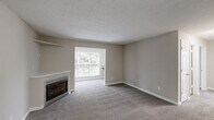 Located at 1720 Old St. Marks Church Rd in Burlington, NC, this single-floor, 2-bedroom, 2-bathroom home offers a well-organized layout with comfortable living spaces throughout. The open living room is a welcoming focal point, featuring a fireplace with a built-in shelf above, neutral-toned carpet, textured ceilings, and a large window that fills the room with natural light and offers views of lush greenery outdoors. The kitchen is thoughtfully appointed with rich dark wood cabinetry, light granite-style countertops, light wood-look flooring, and a full suite of black appliances including a refrigerator, range, microwave, and dishwasher. Both bedrooms are carpeted and feature ceiling fans with light kits and windows that bring in natural light. The spacious primary bedroom includes convenient access to an adjacent bathroom. A dedicated office and a laundry room add functional versatility to the floor plan. Four closets throughout the home provide ample storage. Both bathrooms are finished with clean white tub-shower combos and chrome fixtures. The neutral color palette and consistent finishes throughout create a cohesive, move-in-ready atmosphere.