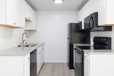 This single-floor unit at 5813 N Garrett St in Garden City, Idaho, presents a clean, neutral aesthetic throughout. The layout connects a well-lit living area to a galley-style kitchen, creating a functional flow between spaces.

The kitchen is outfitted with white cabinetry extending to the ceiling for ample storage, gray countertops, a single-basin sink, subway tile backsplash, and a full suite of black appliances including a refrigerator, electric range, over-the-range microwave, and dishwasher. Light wood-look flooring runs through the kitchen and living areas.

The living room receives generous natural light through a wide multi-pane window and features baseboard heating along the perimeter. A wall-mounted air conditioning unit provides additional climate control. Textured ceilings are present throughout the unit.

The bedrooms are carpeted and each include windows with blinds and baseboard heaters. One bedroom features a ceiling fan with integrated lighting. The bathroom includes a full tub-shower combination with chrome fixtures, a white vanity, and wood-look flooring.

Overall, the unit offers a bright, move-in-ready environment with a straightforward, practical layout suited for everyday living.