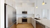 This single-floor residence in Weymouth, MA offers a clean, modern aesthetic throughout its thoughtfully designed layout. The kitchen is a standout feature, showcasing a two-tone cabinetry scheme with sleek white upper cabinets and light wood-grain lower cabinets, complemented by a classic white subway tile backsplash and light-toned quartz countertops. Stainless steel appliances, including a range, over-the-range microwave, refrigerator, and dishwasher, complete the space, while pendant lighting adds a refined touch.

Warm hardwood-style flooring flows consistently through the living areas and bedrooms, creating a cohesive and inviting atmosphere. The living area is bright and open, with crisp white walls and generous natural light. Bedrooms are well-proportioned, featuring large windows that frame outdoor views and allow sunlight to fill the rooms. One bedroom includes access to a walk-in closet with built-in shelving.

Two bathrooms mirror the home's modern design language, each featuring light wood-grain vanities, white quartz countertops, large-format tile flooring, and mirrored vanity lighting. One bathroom includes a tiled soaking tub with a handheld shower, while the second offers a spacious vanity layout. Together, these spaces deliver a fresh, contemporary living environment in a convenient Weymouth location.