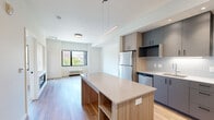Located at 435 Alexander Loop in Eugene, Oregon, this thoughtfully designed one-bedroom, one-bathroom unit offers a modern living experience across a single floor. The open-concept layout connects the kitchen and living room seamlessly, creating an efficient and inviting atmosphere throughout.

The kitchen is a standout feature, outfitted with stainless steel appliances including a gas range with a stainless hood, refrigerator, and dishwasher. Two-tone cabinetry in warm wood and muted gray tones pairs with a tile backsplash and clean white countertops. A central island with a quartz-style surface and built-in shelving provides additional prep space and storage. Sleek linear pendant lighting above the island adds a contemporary touch.

The living room features hardwood-style flooring, large windows that invite generous natural light, and direct access to a private balcony overlooking the surrounding neighborhood's green trees and buildings. The bedroom is carpeted and offers a sizable window with a balcony view, providing a bright and comfortable retreat. A walk-in closet is accessible from the hallway.

The bathroom is clean and modern, featuring a full soaking tub with white subway tile surround and chrome fixtures. Hardwood-style flooring continues through the hallway, tying the unit together cohesively. The overall aesthetic is contemporary, light-filled, and efficiently organized.