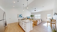 Located at 660 Aubrey Ln in Calabash, NC, this well-designed single-story home offers 2 bedrooms and 2 bathrooms within a thoughtfully laid-out floor plan. The heart of the home is an open-concept living, dining, and kitchen area highlighted by soaring vaulted ceilings and light wood-look flooring. The kitchen features white shaker cabinetry, granite countertops, stainless steel appliances, and a generously sized island with bar seating — ideal for both everyday living and entertaining. Pendant lighting and a ceiling fan complement the bright, airy atmosphere created by ample natural light from multiple windows. A wide hallway with barn door accents connects the private quarters, where both bedrooms offer vaulted ceilings and ample closet space. The primary bathroom includes a dual-sink vanity with white cabinetry and matte black hardware, while the second bathroom mirrors the same clean, modern aesthetic. Throughout the home, crisp white walls and black hardware details provide a cohesive coastal-modern style. Additional spaces include a pantry, laundry area, utility room, patio, and a garage, offering practical functionality to complement the refined interior design.