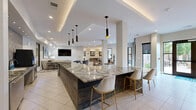 Located at 2200 Aureum Drive in Franklin, Tennessee, this expansive single-floor amenity space delivers a refined, contemporary environment designed for both socializing and focused work. The layout flows seamlessly across several distinct zones, each thoughtfully appointed with high-end finishes and curated décor.

The central living area serves as the heart of the space, anchored by a stunning marble double-sided linear fireplace that elegantly divides the lounge from a dining area. A sculptural chandelier, layered area rugs, and rich wood furnishings contribute to a warm yet modern ambiance. Adjacent, a spacious game room features a full-size billiards table, wall-mounted screens, and a built-in bar-height counter with seating — ideal for recreation and casual gatherings.

A dedicated lounge area showcases plush gold upholstered chairs arranged around small accent tables, with large windows framing views of the lush outdoor surroundings. Nearby, a well-equipped coffee and refreshment bar features granite countertops, stainless steel appliances, and a bold geometric-patterned tile backsplash.

The private office area includes individual workstations enclosed by glass-paneled walls, offering focused work environments. One pod features a striking vintage microphone mural, adding a nod to Franklin's rich musical heritage. Recessed lighting, large-format tile flooring, and neutral tones unify the entire space with a polished, cohesive aesthetic.