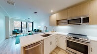 Located at 487 48th St in Oakland's Temescal neighborhood, this single-floor unit showcases a contemporary design with light wood flooring, clean white walls, and modern finishes throughout. The open-concept layout connects the kitchen and living areas, creating a cohesive and functional living space.

The kitchen is well-appointed with stainless steel appliances, including a gas range, built-in microwave, dishwasher, and refrigerator. A large peninsula with a white quartz countertop provides additional workspace and casual seating. Upper cabinetry in a warm natural wood tone contrasts with the crisp white lower cabinets, while a white penny-tile backsplash adds texture and detail.

The living area is bright and welcoming, with large black-framed windows and a glass door that opens to a private balcony, offering outdoor views and ample natural light.

The unit includes two bedrooms, both featuring light wood flooring and windows that bring in natural light. One bedroom includes a dedicated desk area, offering a functional workspace.

The bathroom features large-format neutral tile flooring, a tiled walk-in shower, a light wood vanity with open shelving, and a well-lit mirror, maintaining the unit's clean, modern aesthetic throughout.