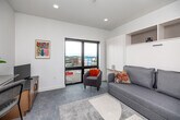 This efficiently designed single-floor unit offers a thoughtfully organized layout that maximizes every square foot. The galley-style kitchen is a standout feature, outfitted with dual-tone cabinetry — combining dark upper cabinets with warm wood lower cabinetry — sleek dark countertops, a dark tile backsplash, and a full suite of stainless steel appliances including a refrigerator, microwave, and cooktop. Recessed lighting runs the length of the corridor, creating a bright and clean aesthetic throughout.

The main living space is smartly designed around a built-in murphy bed system with integrated white cabinetry and open shelving, allowing the room to serve as both a lounge and sleeping area. A sofa sits in front of the murphy bed, and a large floor-to-ceiling window floods the room with natural light while offering open city views. A wall-mounted mini-split system provides climate control.

The bathroom features warm wood cabinetry, a granite-topped vanity with a large mirror, black hardware accents, and neutral tile flooring — creating a clean, contemporary feel. A dedicated laundry room rounds out the unit, complete with a full-size front-loading washer and dryer, wire shelving, and ample wall space for storage. Consistent light-toned flooring throughout ties the entire space together cohesively.