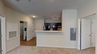 This single-floor, two-bedroom, one-bathroom unit offers a practical and comfortable layout designed for everyday living. The living area features neutral-toned carpet and transitions into a kitchen finished with hardwood-style flooring. The kitchen is outfitted with dark cabinetry, black appliances, and a peninsula breakfast bar that opens toward the living space, creating an accessible, open-concept feel. A track light fixture illuminates the kitchen area, while a textured ceiling adds architectural detail throughout the common areas.

Both bedrooms are carpeted and include ceiling fans with light fixtures, providing comfort year-round. Each room receives natural light through windows fitted with blinds. The larger bedroom includes an adjoining door, likely leading to a closet or additional storage. The bathroom features a dark vanity with a white countertop, hardwood-style flooring, and a tub-shower combination. A dedicated laundry closet houses a full-size front-loading Whirlpool washer and dryer set, adding significant in-unit convenience. Neutral gray walls throughout contribute to a clean, cohesive aesthetic.