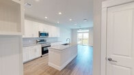 This thoughtfully designed 1-bedroom, 1-bathroom unit offers a modern, open-concept layout that maximizes its efficient footprint. The kitchen serves as the centerpiece of the living space, showcasing white shaker cabinetry, granite countertops, a subway tile backsplash, and a full suite of stainless steel appliances including a French door refrigerator, electric range, and built-in microwave. A central island with an undermount sink provides additional prep space and flows seamlessly into the living area, which is illuminated by recessed lighting and a ceiling fan. Light wood-style flooring extends throughout the main living areas, lending a clean, contemporary feel. Sliding glass doors open from the living room onto a private balcony with striking city skyline views. The bedroom features plush carpet, a ceiling fan, and a window with outdoor views, as well as access to a dedicated closet. The bathroom is finished with a frameless glass-enclosed walk-in shower clad in large-format marble-style tile, a granite-topped vanity, and matching wood-look flooring. Neutral tones and abundant natural light throughout create a bright, inviting atmosphere.