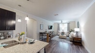 This single-floor residence offers a thoughtfully designed open-concept layout that seamlessly connects the kitchen, dining, and living areas. The kitchen is a standout feature, equipped with dark espresso cabinetry, stainless steel appliances, track lighting, and a granite-topped peninsula with bar seating — ideal for casual dining or entertaining. An arched passageway adds an architectural touch, guiding the eye toward the dining area and spacious living room beyond. The living room is finished with rich hardwood-style flooring, crown molding, a ceiling fan, and ample natural light from large windows dressed with neutral curtains. Two well-sized bedrooms are carpeted for comfort, each featuring multiple windows that invite natural light and outdoor views. The dedicated office space includes hardwood-style flooring and a bright window, offering a functional and quiet work-from-home environment. Both bathrooms are finished with marble-style subway tile surrounds accented by decorative mosaic tile borders, granite vanity tops, and dark wood cabinetry. The cohesive design throughout — neutral tones, quality finishes, and a balanced mix of hard and soft surfaces — creates a warm, livable atmosphere from room to room.
